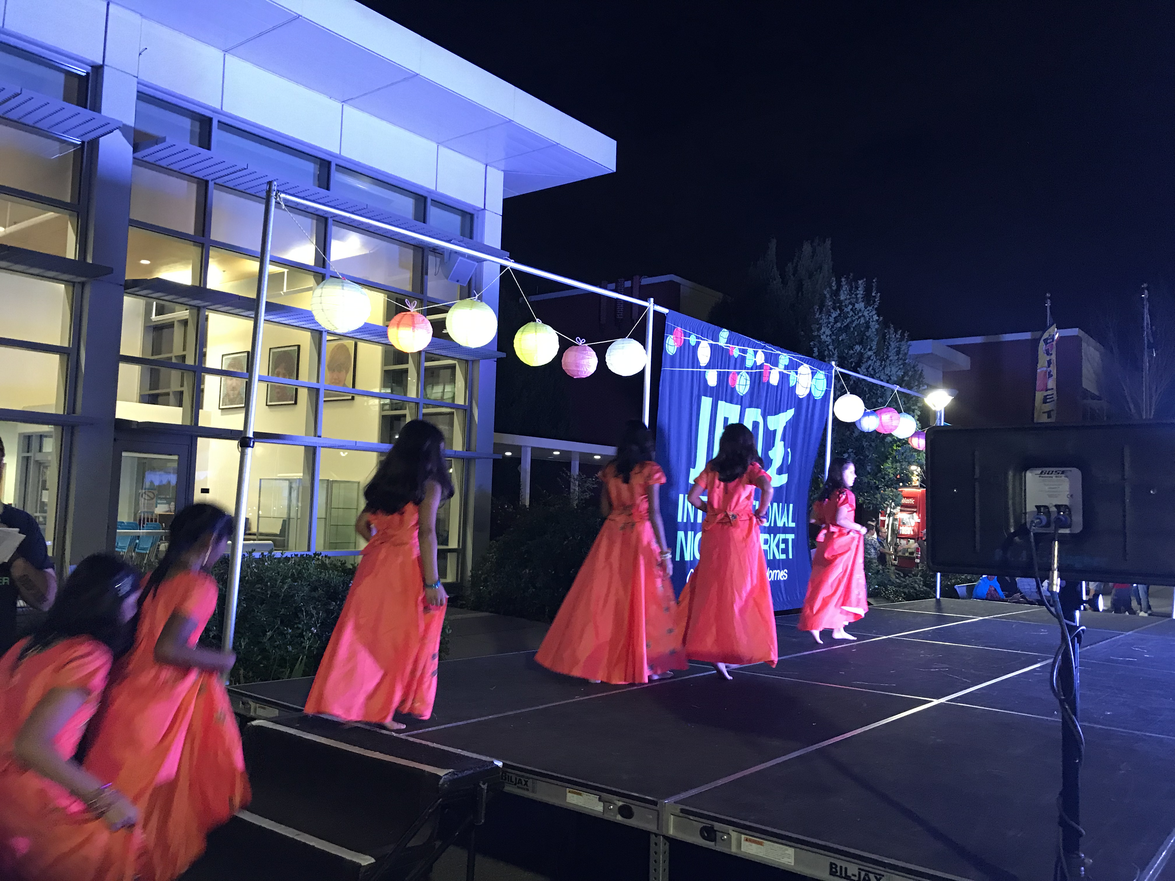 Dancers in bright orange costumes performing on an outdoor stage at night